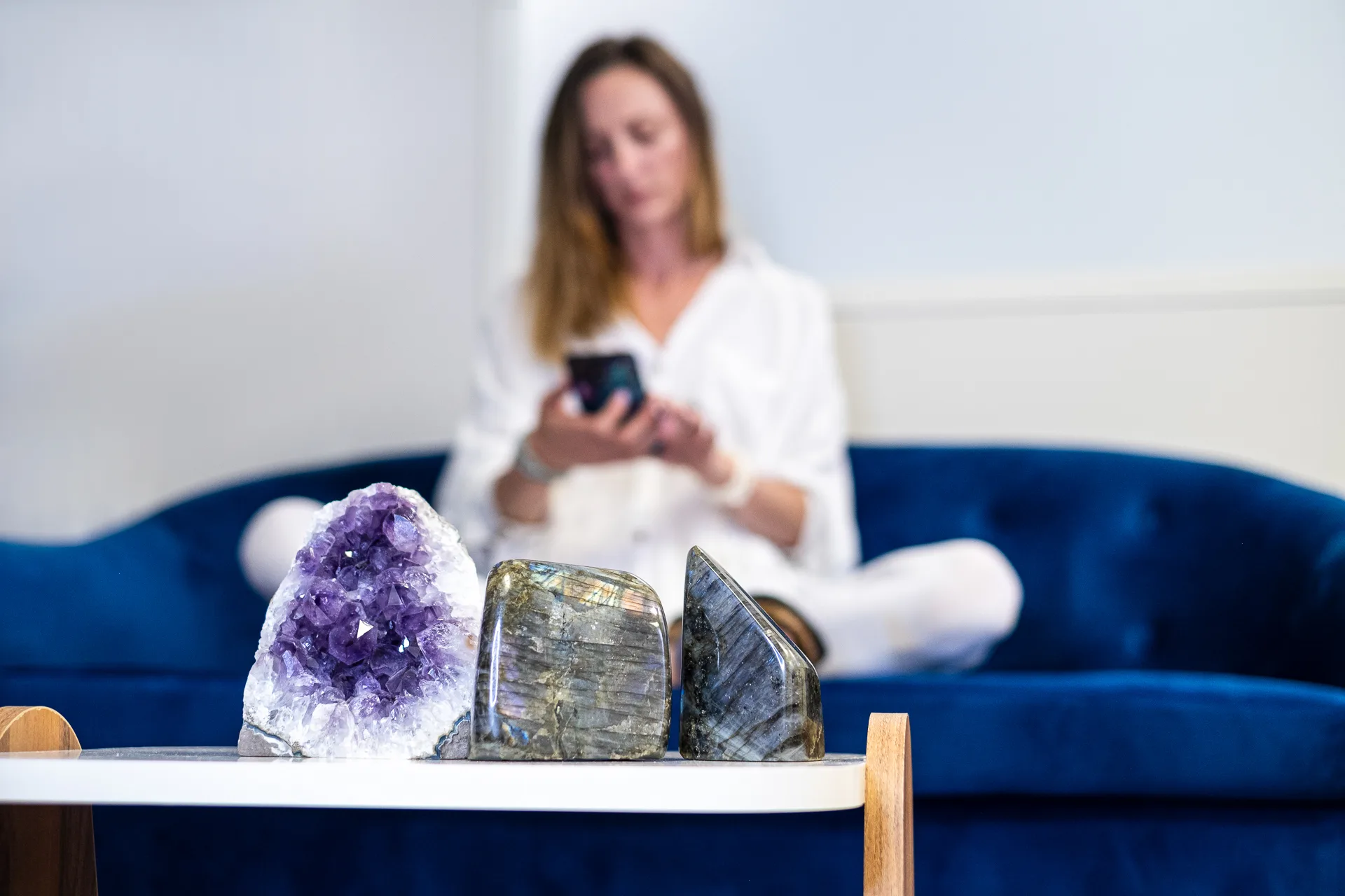 Pierres et minéraux naturels exposés sur une table, avec une femme assise en arrière-plan dans une boutique de lithothérapie.