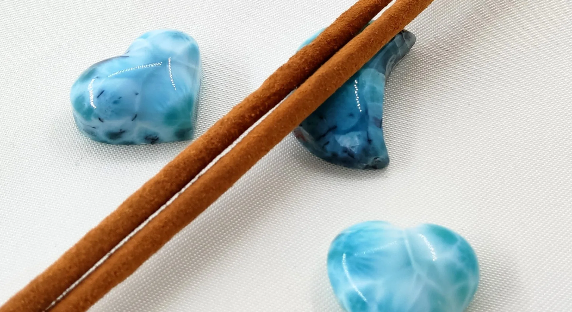 Cœurs en pierres de larimar sur tissu blanc et bâtons de cannelle, parfaits pour débuter en lithothérapie avec sérénité et paix intérieure