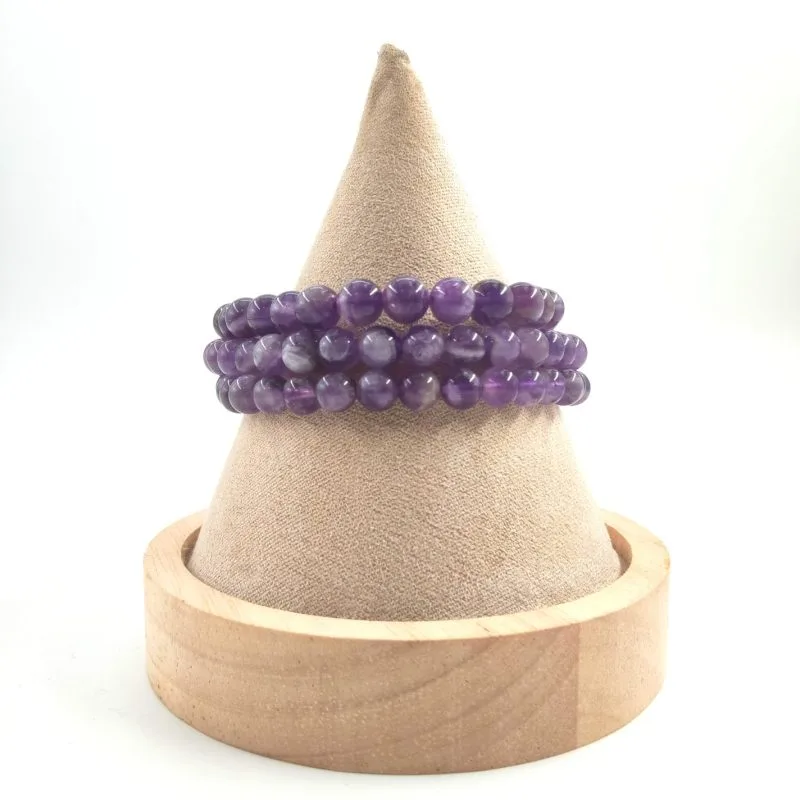 Bracelets en améthyste à perles rondes, exposés sur un présentoir conique en tissu beige avec une base en bois clair.