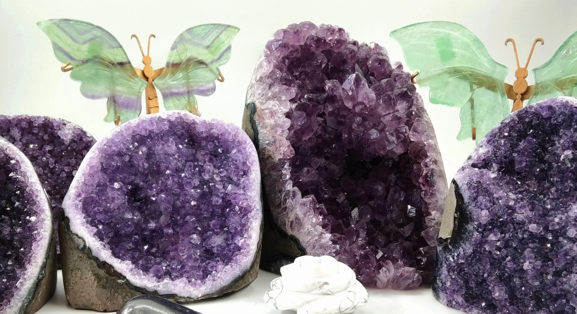 Géodes d'améthyste violette accompagnées de papillons décoratifs en fluorite verte et mauve, avec une sculpture de fleur en howlite blanche au centre