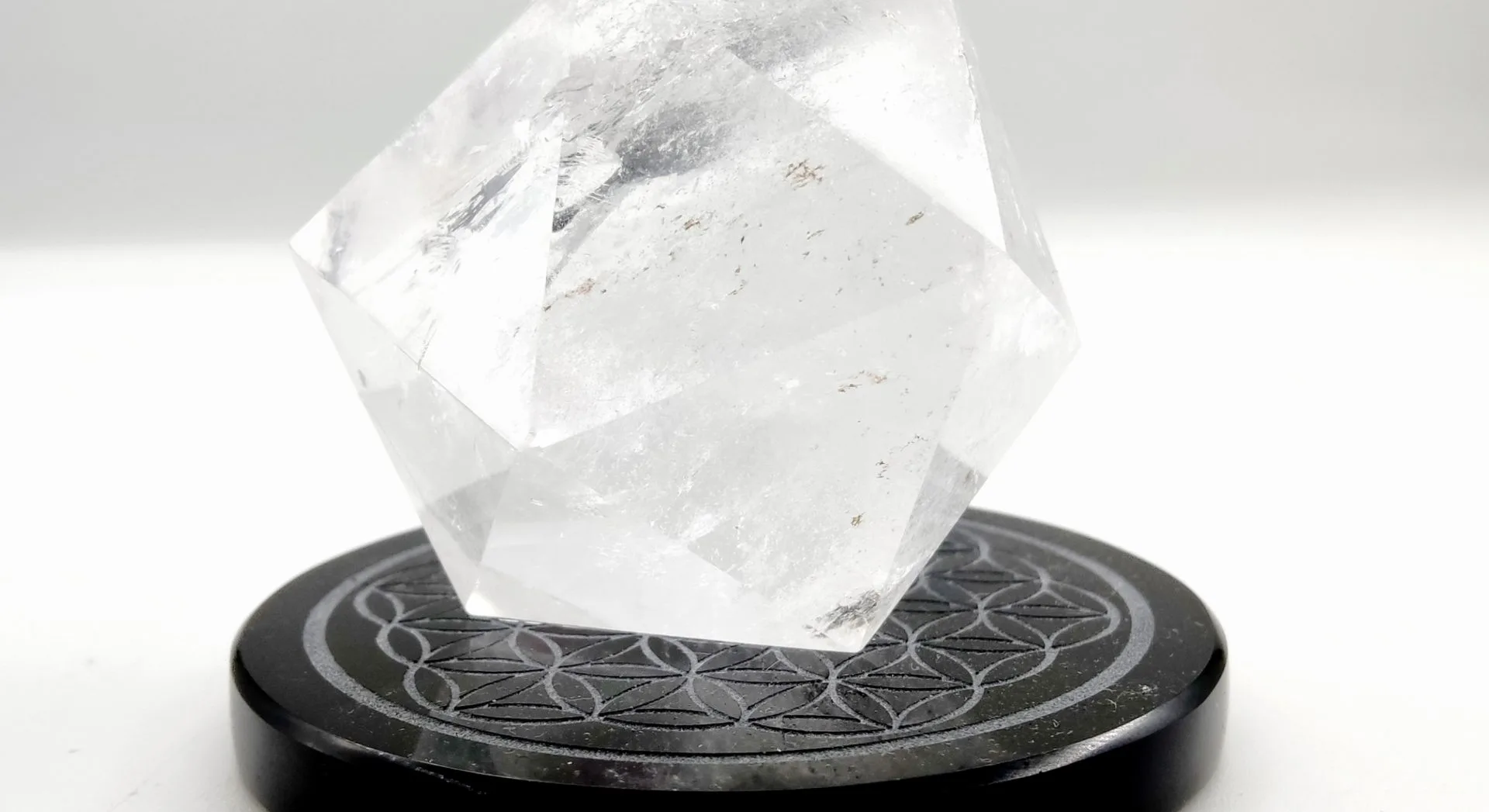 Octaèdre géométrie sacrée en cristal de roche posé sur un socle noir gravé de la Fleur de Vie, utilisé en lithothérapie pour l'harmonisation énergétique.