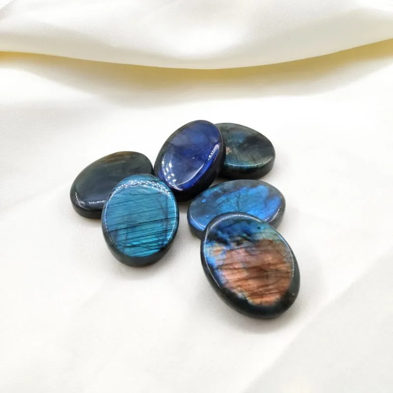 Six pierres polies en labradorite aux reflets irisés bleus et orangés, posées sur un tissu blanc crème.
