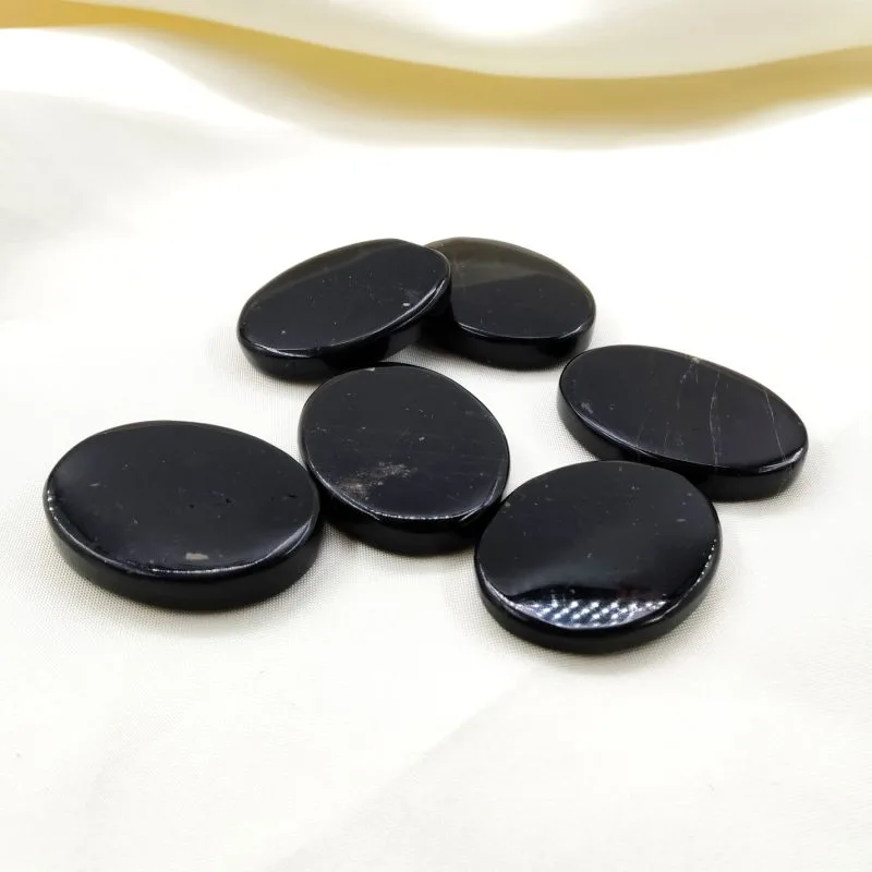 Pierre plate polie en six exemplaires d’un noir profond et brillant avec quelques rares inclusions claires, disposées sur un tissu crème doux.