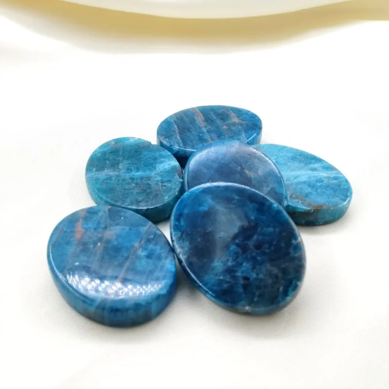 Six pierres polies en apatite bleue aux nuances intenses, disposées sur un tissu blanc crème.