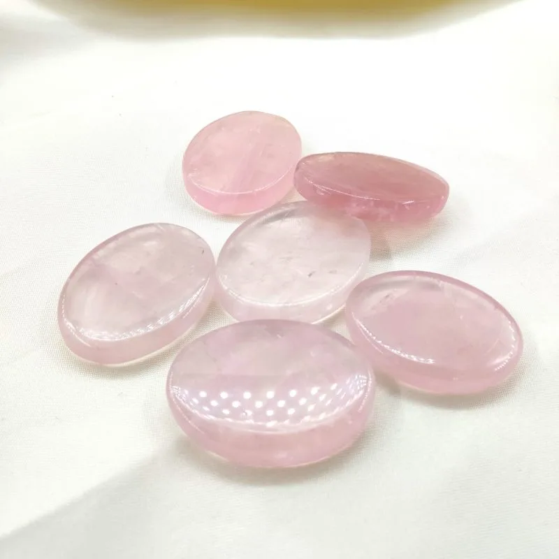 Six pierres polies en quartz rose, aux teintes douces et translucides, disposées sur un tissu blanc crème.