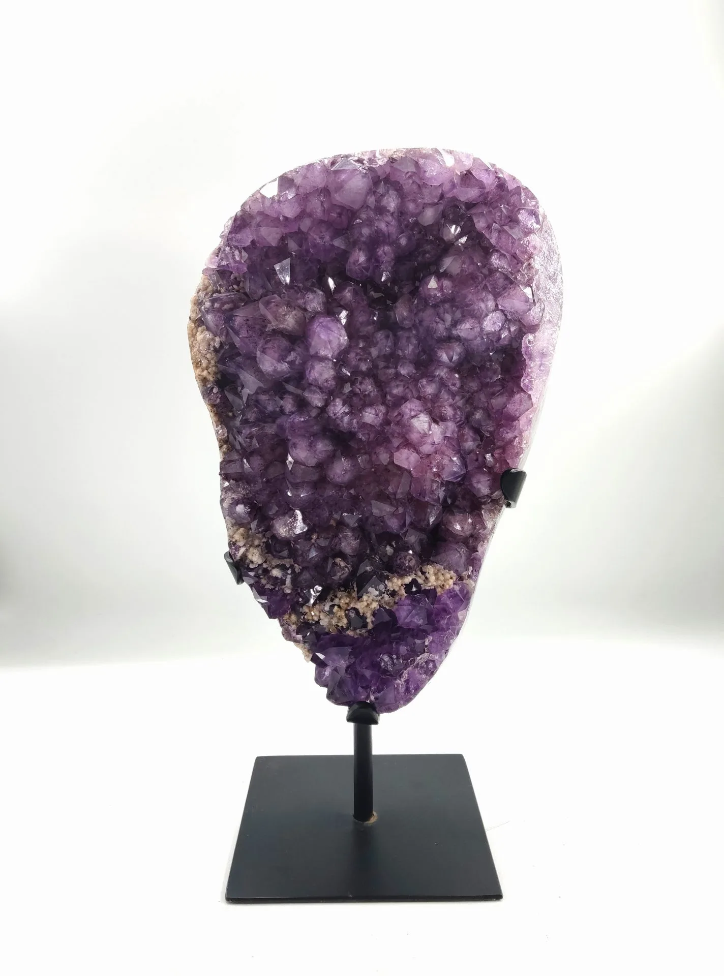 Géode d’améthyste naturelle montée sur un support métallique noir, présentant de nombreux cristaux violets brillants aux reflets translucides, formant une structure minérale éclatante.