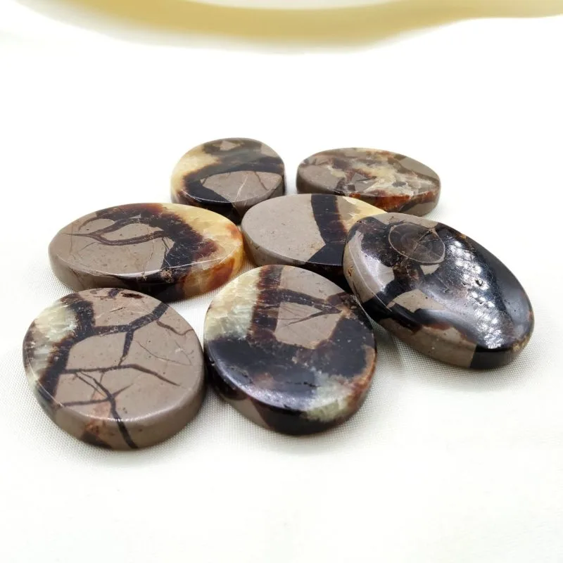 Sept pierres polies en septaria, aux motifs naturels bruns, beiges et crème, disposées sur un tissu blanc crème.