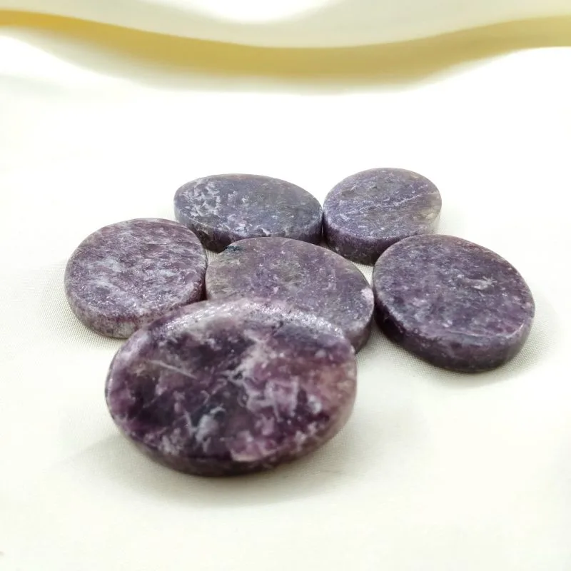 Six pierres polies en lépidolite de couleur violette, disposées sur un tissu blanc crème.