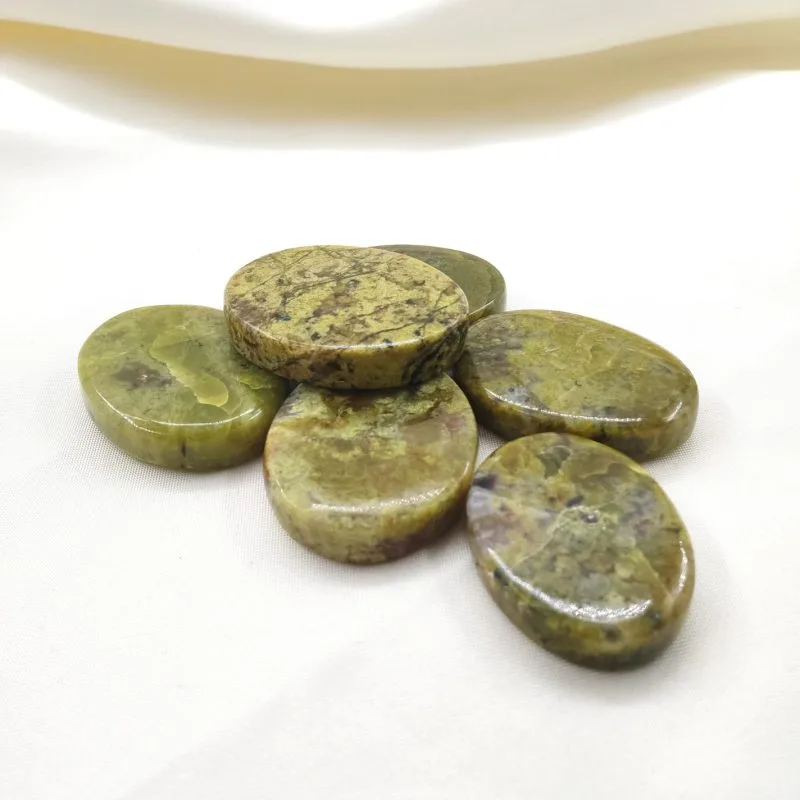 Six pierres polies en serpentine vert olive, aux nuances marbrées naturelles, disposées sur un tissu blanc crème.