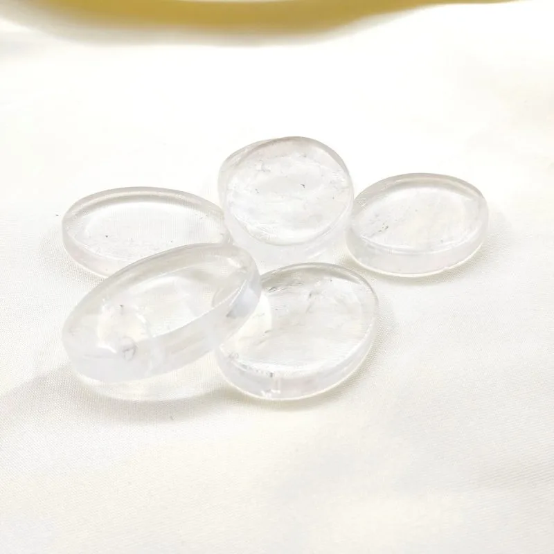 Cinq pierres polies en cristal de roche, translucides et lumineuses, posées sur un tissu blanc crème.