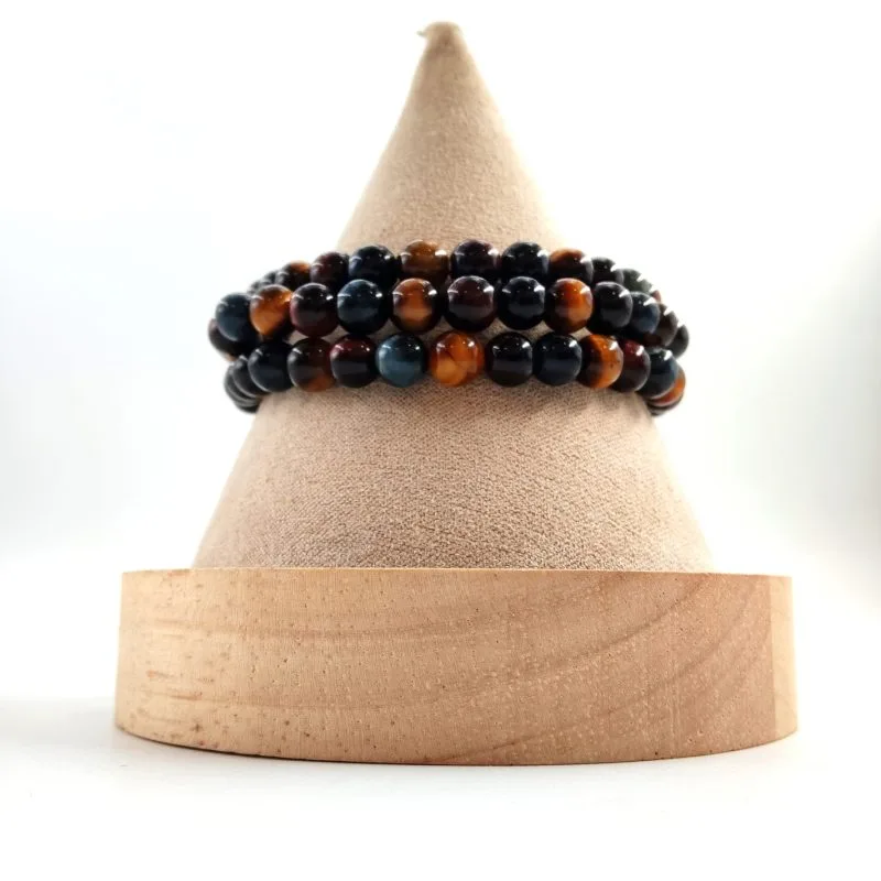 Bracelet en perles rondes de pierre œil de tigre multicolore (doré, bleu et rouge), présenté sur un support conique recouvert de tissu beige avec base en bois clair.