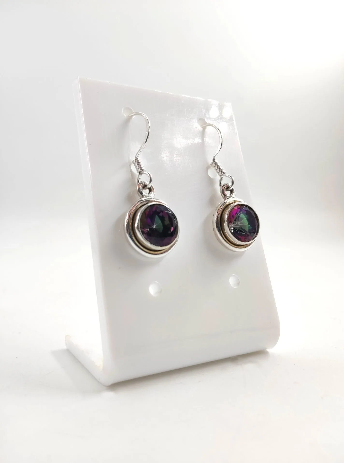 Paire de boucles d’oreilles pendantes en argent, ornées de pierres rondes facettées aux reflets multicolores violet et vert, présentées sur un support blanc.