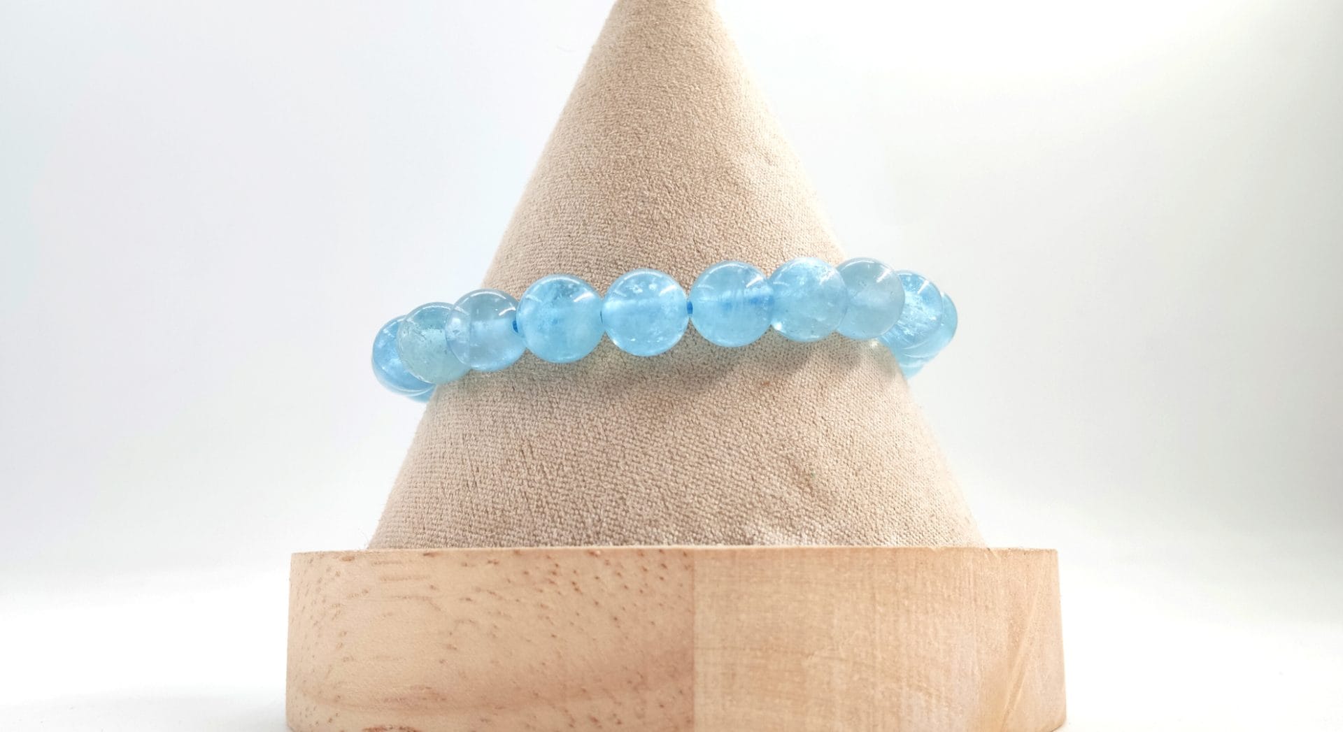 Bracelet en perles rondes d’aigue-marine bleue, présenté sur un cône d’exposition en tissu beige avec base en bois, sur fond clair.