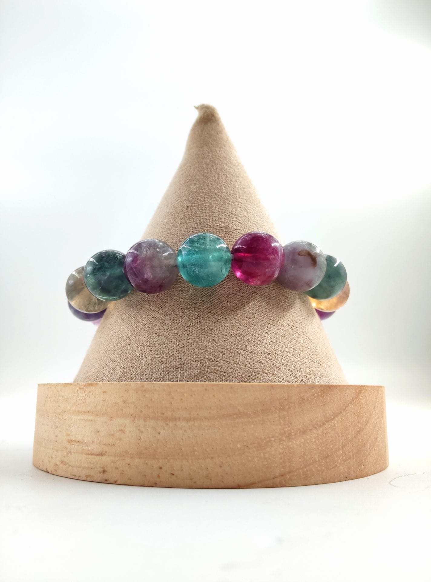 Bracelet en perles rondes de fluorite multicolore, aux nuances de vert, violet, rose et jaune, présenté sur un cône en tissu beige avec base en bois clair.