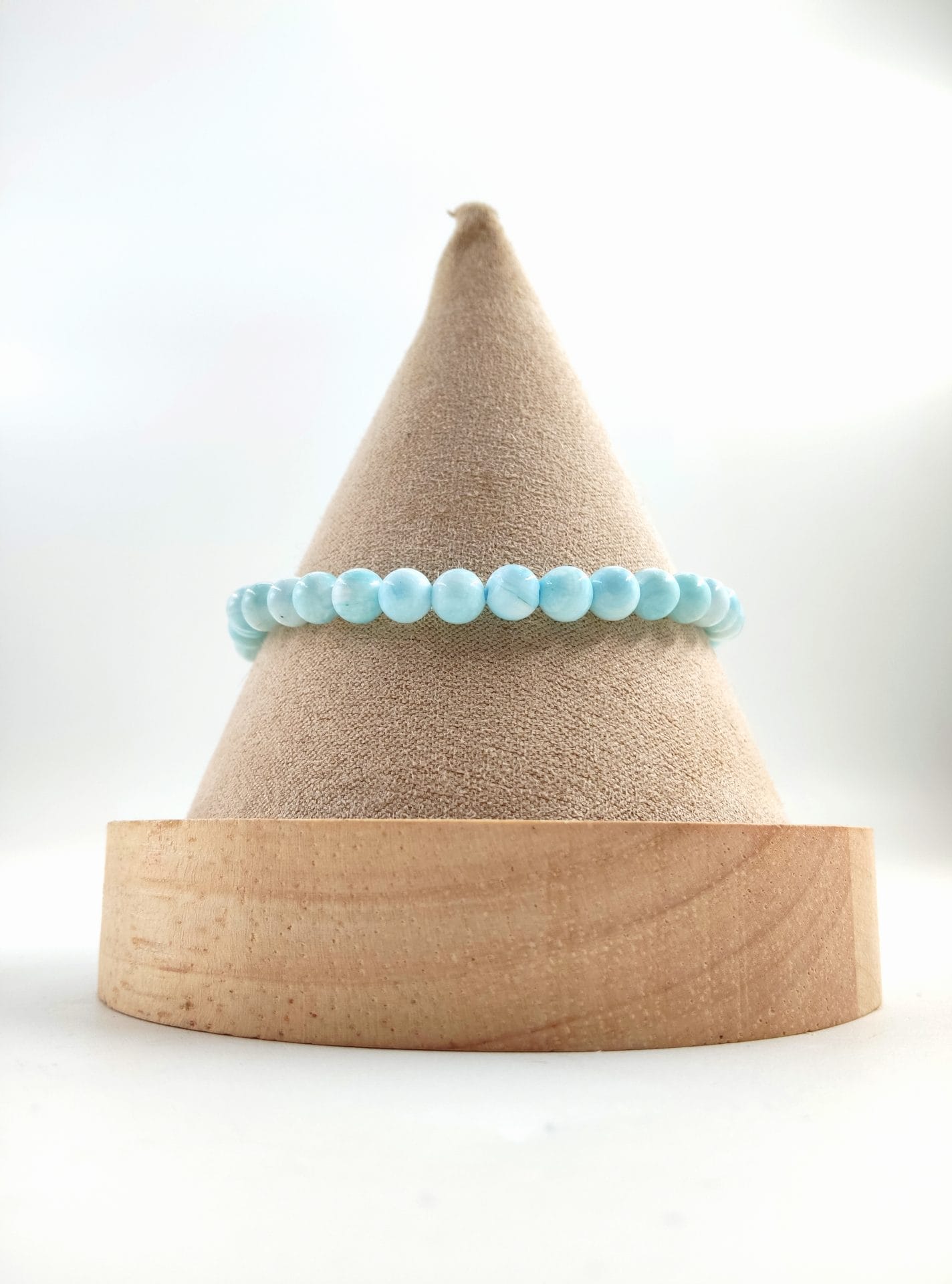 Bracelet en perles rondes d’hémimorphite bleu ciel, aux reflets doux et légèrement marbrés, présenté sur un cône en tissu beige avec base en bois clair.