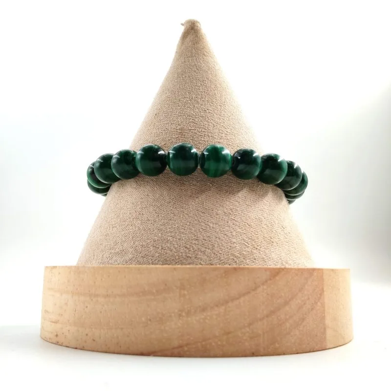 Bracelet en perles rondes de malachite, aux nuances vert foncé et motifs naturels en bandes concentriques, présenté sur un cône en tissu beige avec base en bois clair.