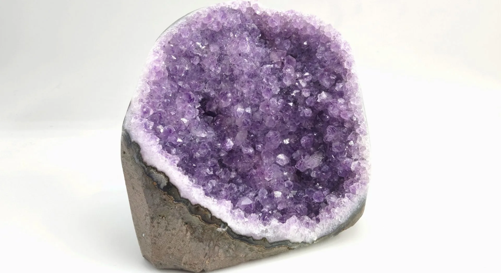Géode d’améthyste violette, aux cristaux brillants et scintillants à l’intérieur, présentée sur fond blanc.