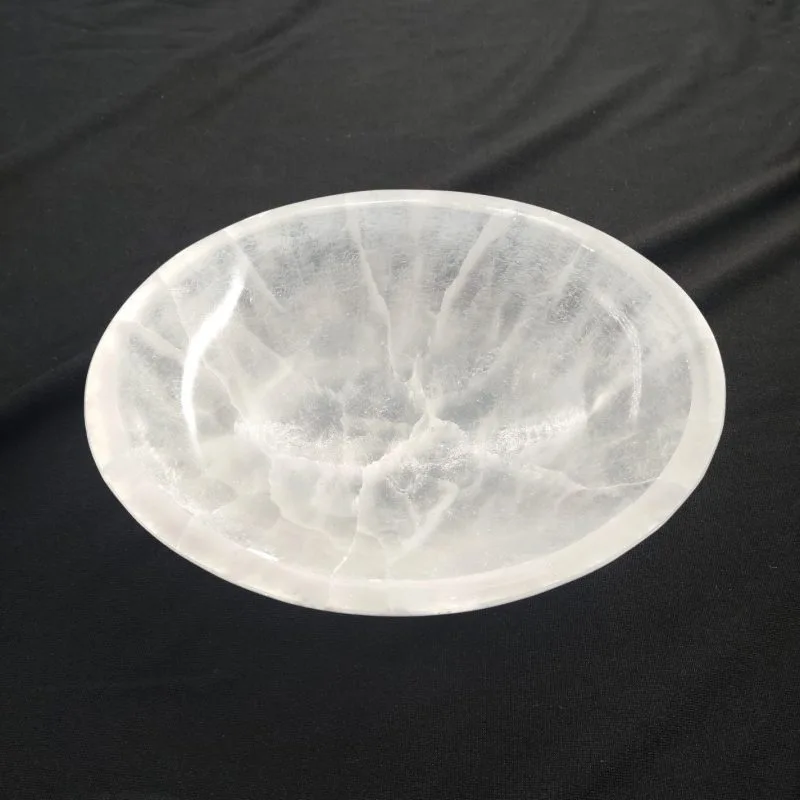 Grand bol rond en sélénite blanche, translucide et striée de reflets lumineux naturels, posé sur un tissu noir.