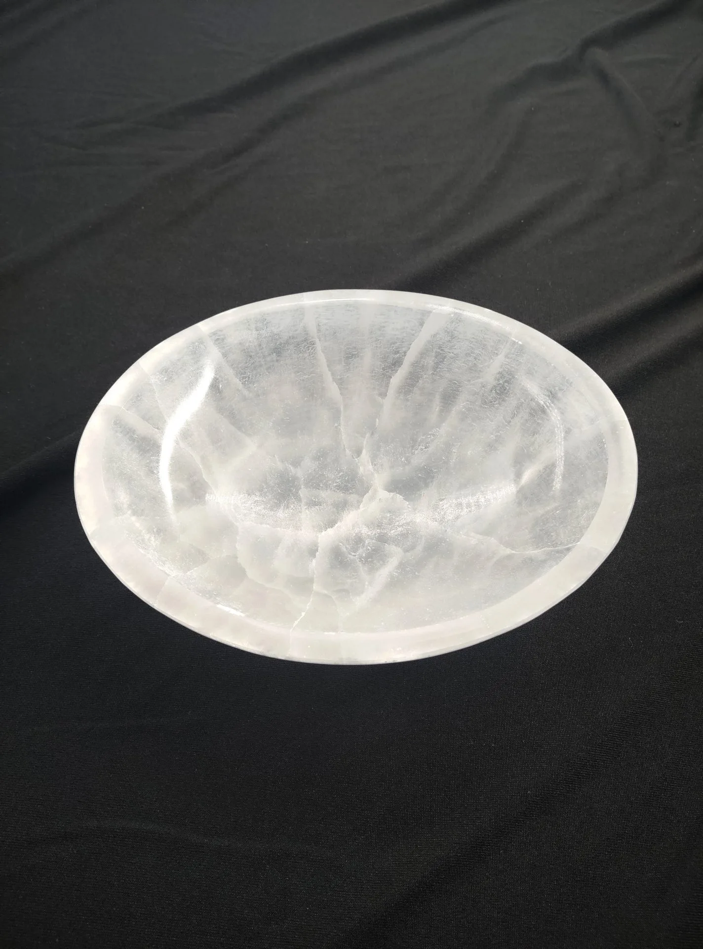 Grand bol rond en sélénite blanche, translucide et striée de reflets lumineux naturels, posé sur un tissu noir.