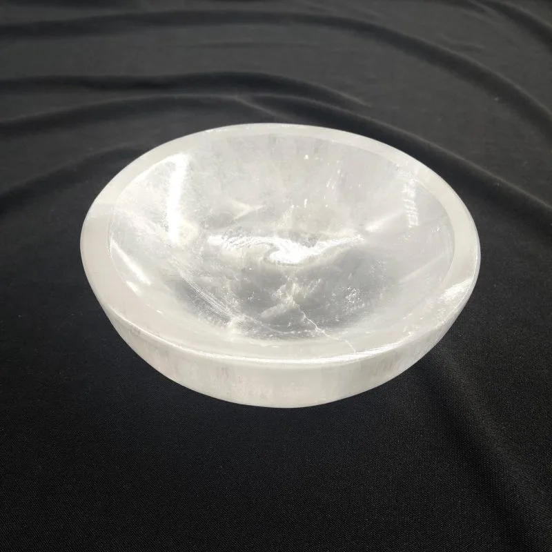 Bol rond en sélénite blanche, translucide et lumineuse, posé sur un tissu noir. La surface laisse voir les stries naturelles et les reflets satinés caractéristiques de la sélénite.