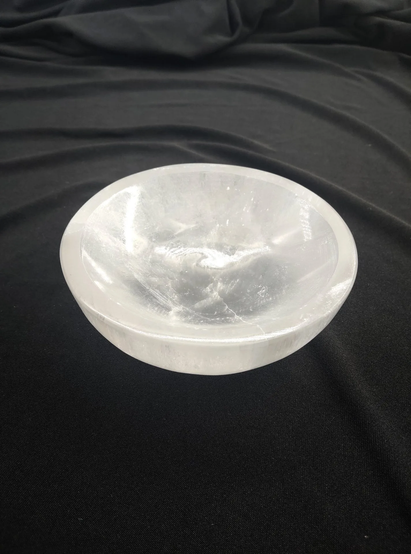 Bol rond en sélénite blanche, translucide et lumineuse, posé sur un tissu noir. La surface laisse voir les stries naturelles et les reflets satinés caractéristiques de la sélénite.