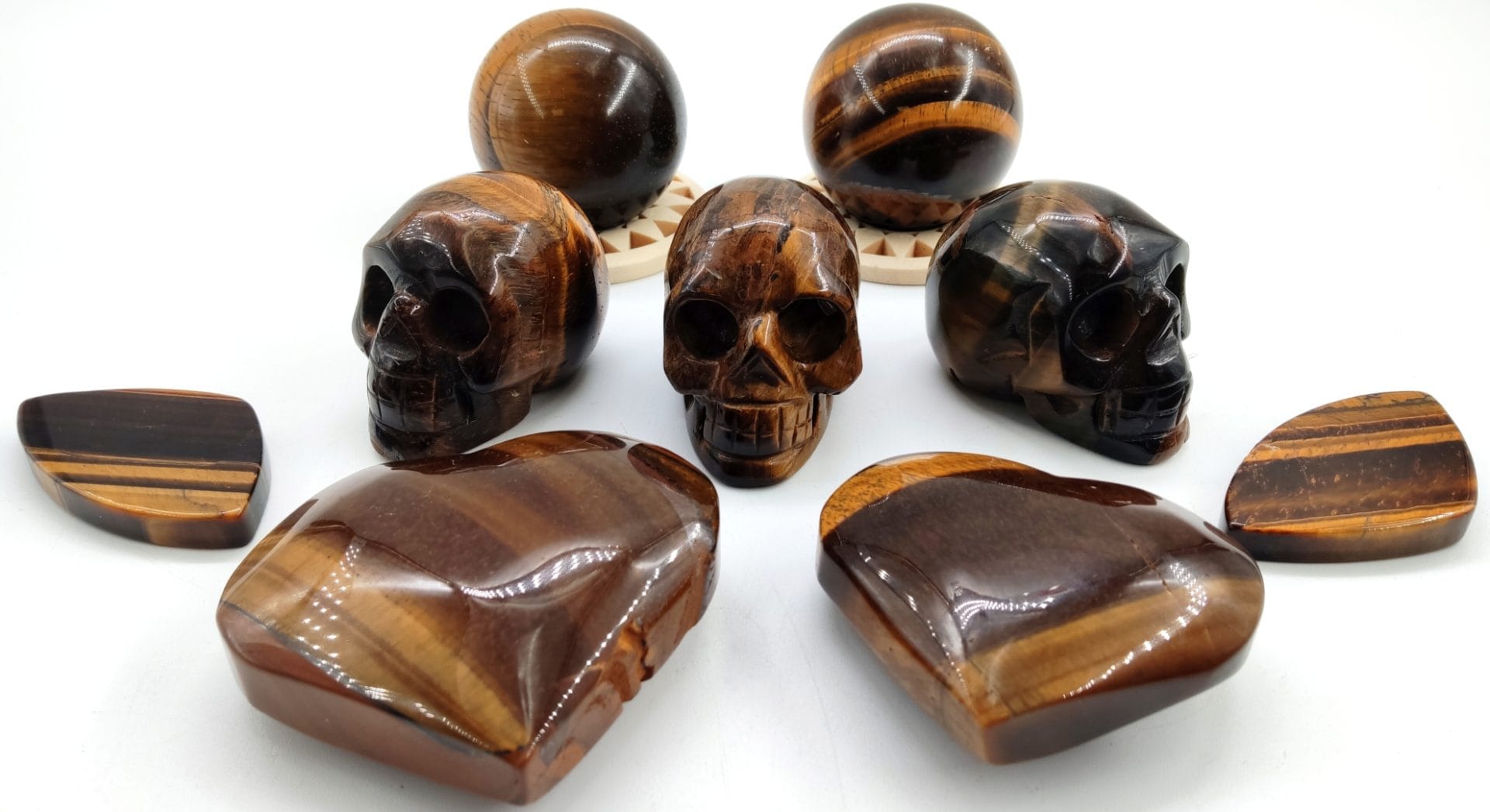 Sculptures en œil de tigre comprenant plusieurs crânes, des sphères polies et des galets aux reflets dorés caractéristiques de cette pierre.