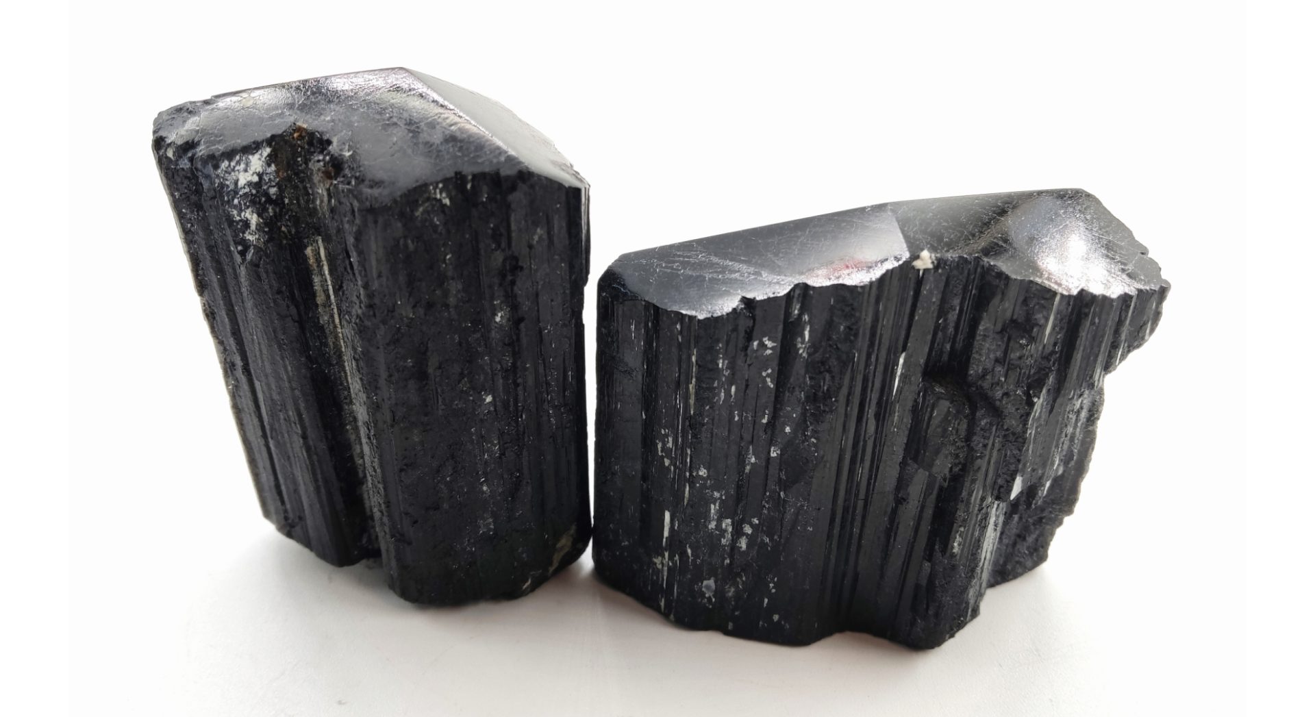Deux morceaux bruts de tourmaline noire, présentant des stries verticales et une surface naturelle brillante.