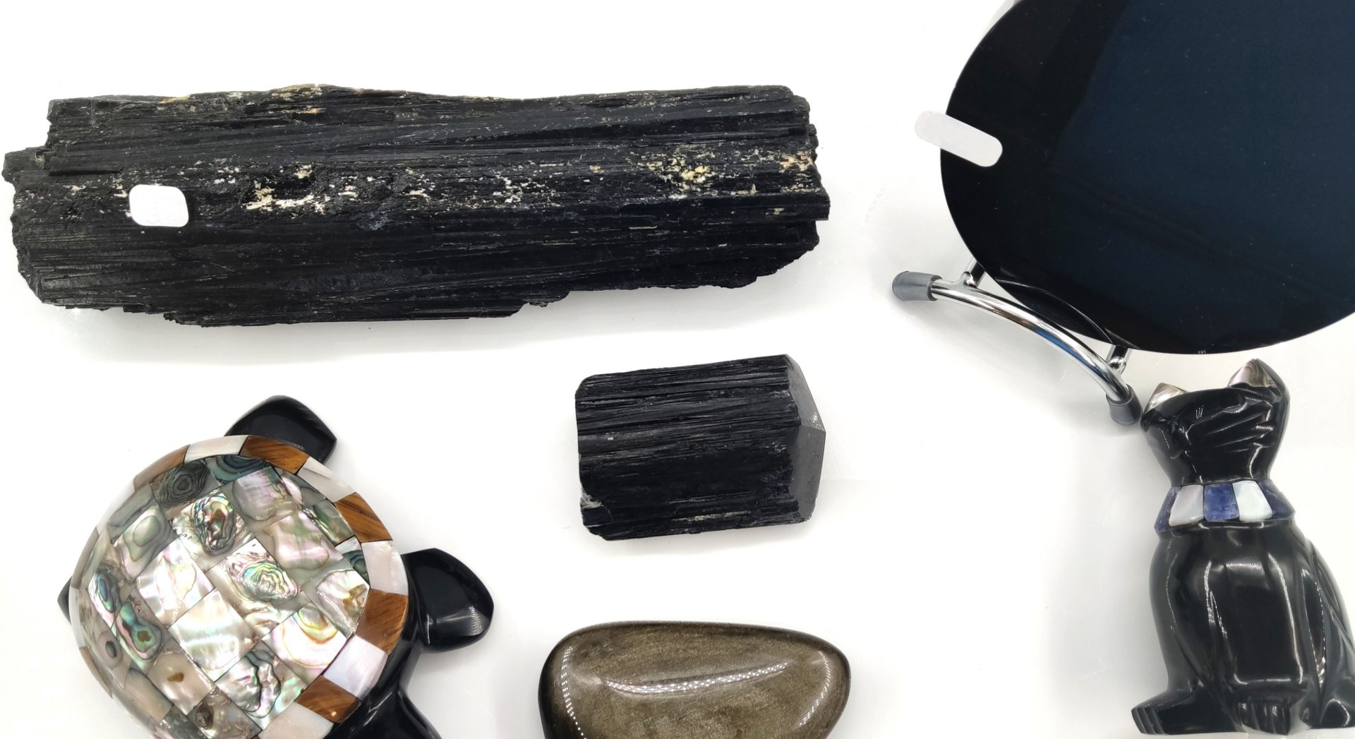 Une collection de pierres noires mates et brillantes, incluant des sculptures, sur un fond blanc uni.